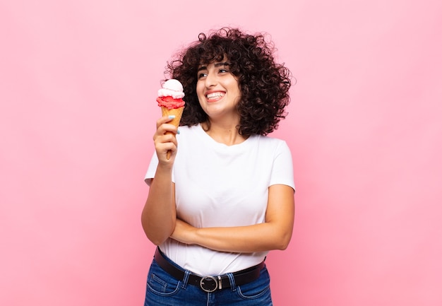 Giovane donna con un gelato che sorride felice e sogna ad occhi aperti o dubita, guardando di lato