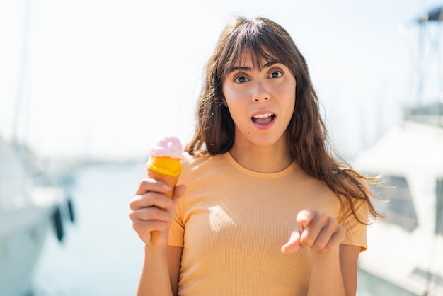 Giovane donna con un gelato cornetta all'aperto sorpreso e puntato davanti