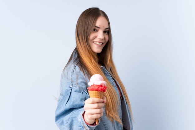 Giovane donna con un gelato di cornetta isolato sulla parete blu con espressione felice