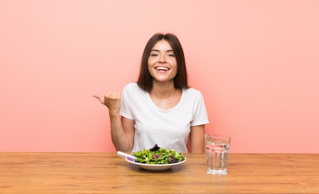 Giovane donna con un'insalata che punta verso il lato per presentare un prodotto