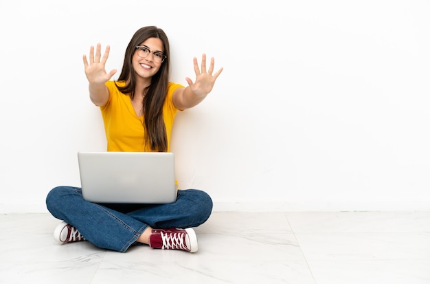 Giovane donna con un laptop seduta sul pavimento che conta dieci con le dita
