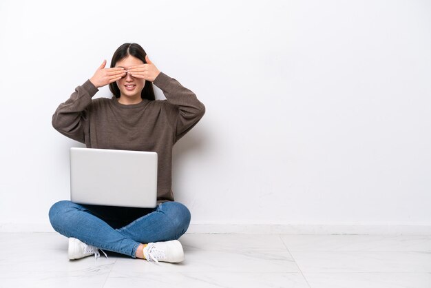 Giovane donna con un laptop seduto sul pavimento che copre gli occhi con le mani