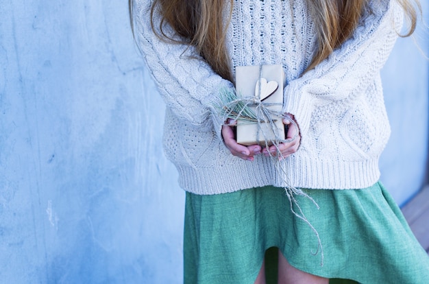 Giovane donna con un maglione lavorato a maglia tiene una confezione regalo in carta artigianale con cuore e ramo di abete