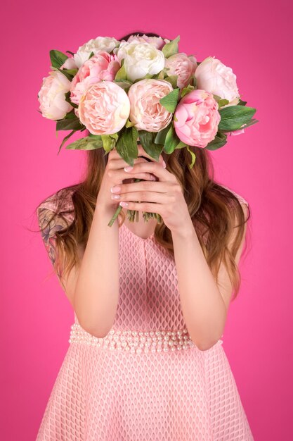 Giovane donna con un mazzo di peonie su sfondo rosa