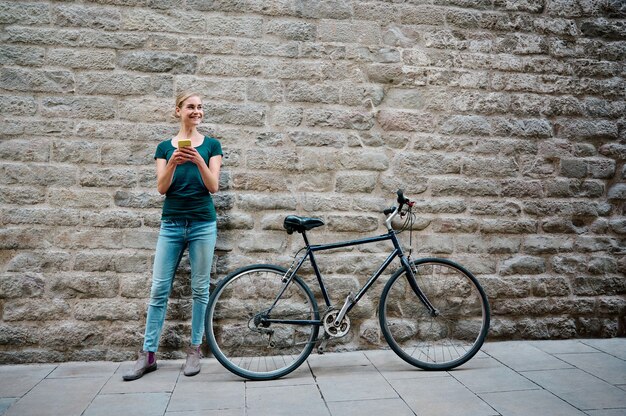 giovane donna con un muro di mattoni dietro di lei con bici e smartphone