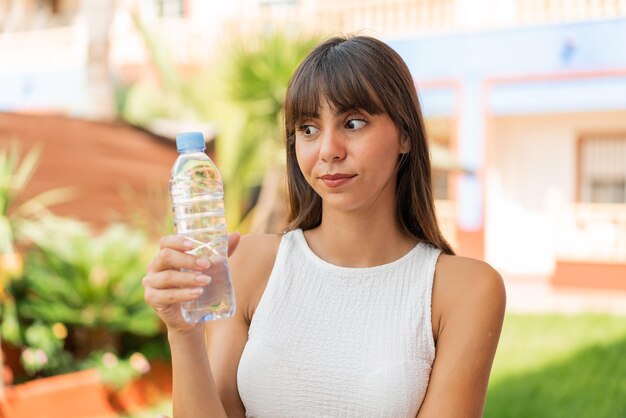 Giovane donna con una bottiglia d'acqua all'aperto con espressione triste