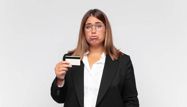 Giovane donna con una carta di credito che si sente triste e piagnucolona con uno sguardo infelice, piange con un atteggiamento negativo e frustrato