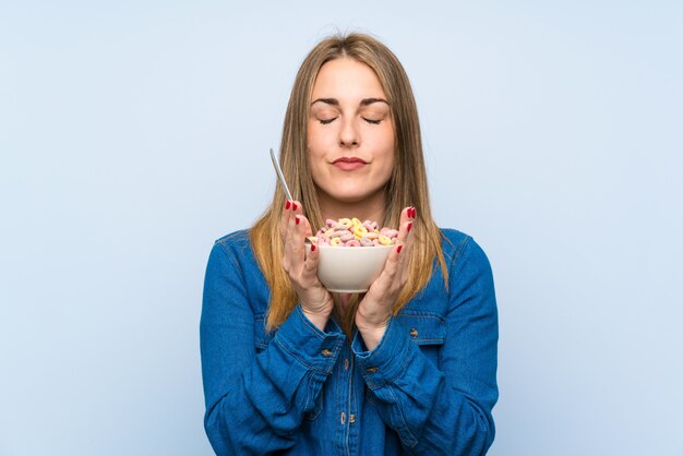 Giovane donna con una ciotola di cereali sopra isolato muro blu