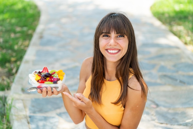 Giovane donna con una ciotola di frutta all'aperto e puntandola