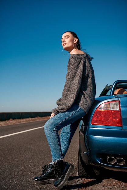 Giovane donna con una coda in piedi vicino a un'auto senza tetto all'aperto