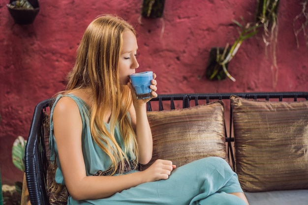 Giovane donna con una colazione mediterranea seduti al divano e bevande Trendy drink Blue latte Hot Butterfly pea latte o spirulina blu latte