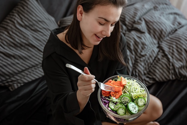 Giovane donna con una grande ciotola di insalata fresca con verdure a letto