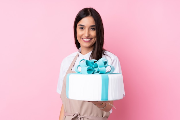 Giovane donna con una grande torta sopra la parete isolata con espressione felice