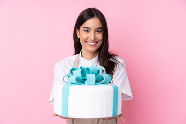 Giovane donna con una grande torta sopra la parete isolata