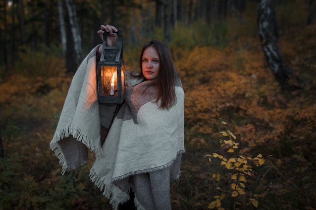 Giovane donna con una lampada a cherosene nella foresta