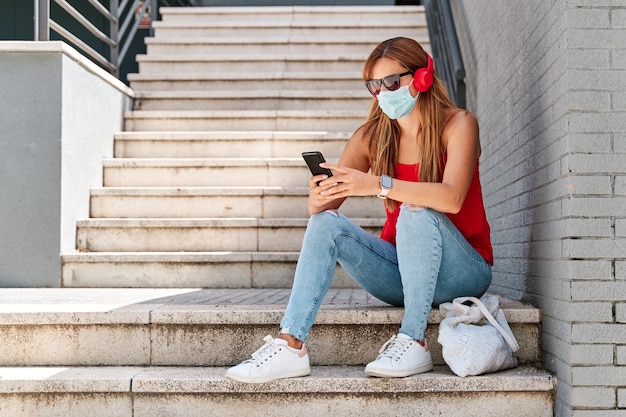 Giovane donna con una maschera utilizzando il suo telefono cellulare in città Concetto di nuova normalità e lotta contro il virus.