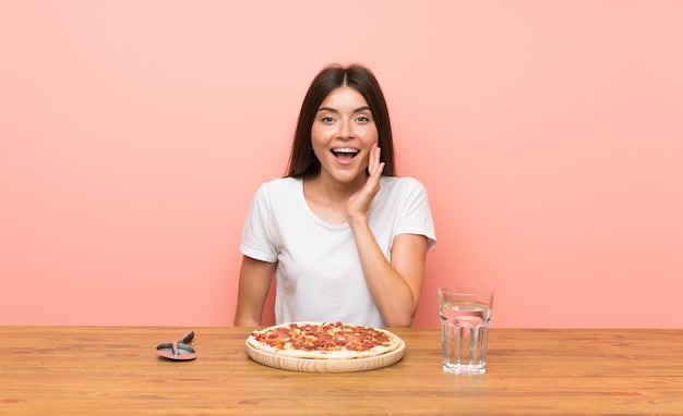 Giovane donna con una pizza con espressione facciale sorpresa e scioccata