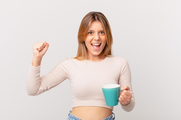 Giovane donna con una tazza da caffè che grida in modo aggressivo con un'espressione arrabbiata