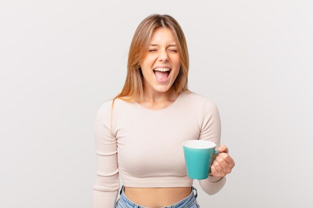 Giovane donna con una tazza da caffè che grida in modo aggressivo, sembra molto arrabbiata