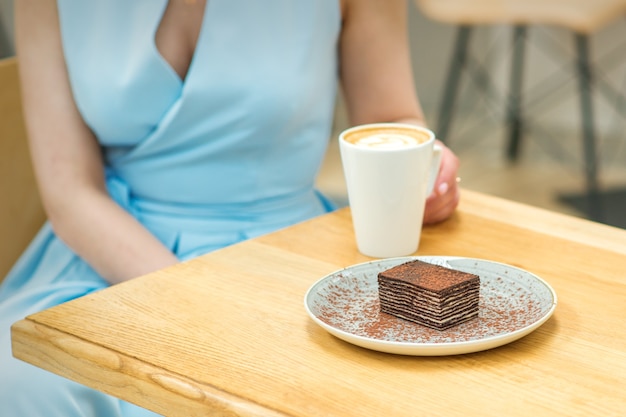 Giovane donna con una tazza di caffè e una fetta di torta seduta al tavolo in un bar all'aperto