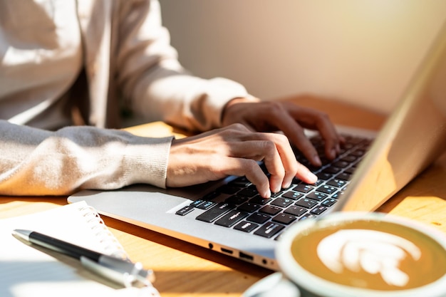 Giovane donna con una tazza di caffè seduta e che lavora al portatile al caffè