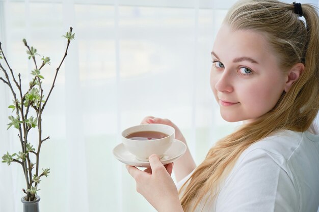 Giovane donna con una tazza di tè in mano si siede vicino allo spazio della finestra per il testo