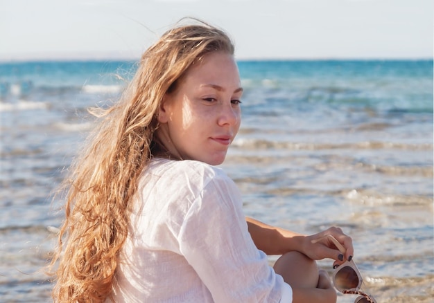 Giovane donna con uno sguardo pensieroso si siede in riva al mare Il concep