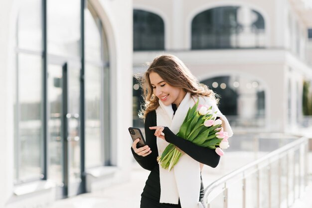 Giovane donna con uno smartphone in mano e fa acquisti online o comunica in un social network mentre cammina per le strade della città