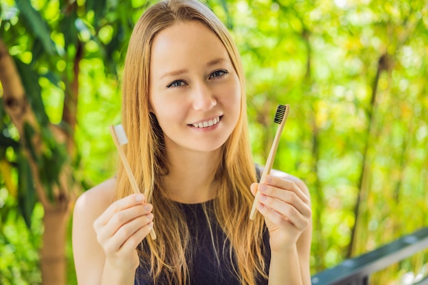 Giovane donna con uno spazzolino da denti di bambù sullo sfondo di bambù verde in crescita