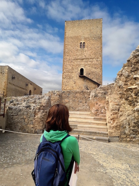 giovane donna con zaino blu guardando la torre di un castello