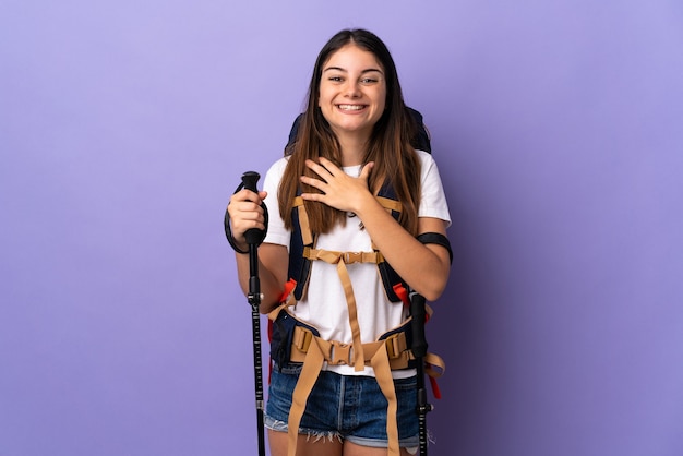 Giovane donna con zaino e bastoncini da trekking isolati su viola sorridente molto