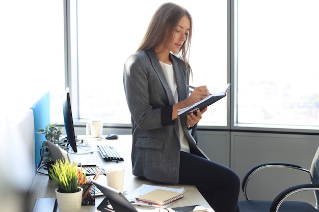 Giovane donna concentrata che scrive qualcosa mentre lavora in ufficio.