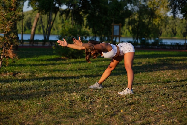 Giovane donna concentrata con una figura atletica che fa pilates e si allena al parco