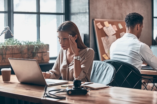 Giovane donna concentrata in abbigliamento casual intelligente che usa il laptop mentre lavora in ufficio