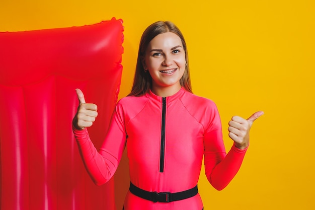 Giovane donna corpo sottile rosa costume intero su materasso ad aria rosa isolato su sfondo giallo brillante studio di colore estate hotel piscina mare vacanza sole abbronzatura concetto posto per il testo