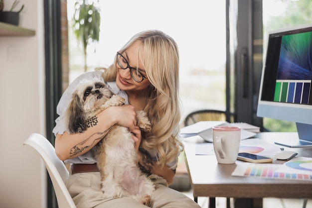 Giovane donna creativa che si diverte con il suo cane mentre lavora nel comfort di casa sua.