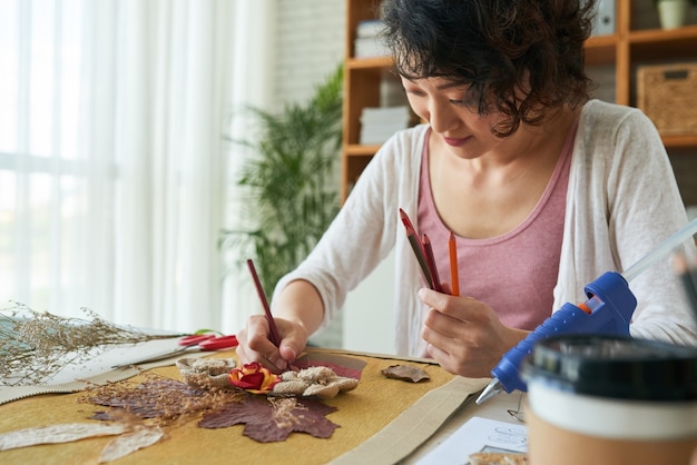 Giovane donna creativa e talentuosa che usa matite colorate per finire la sua foto in stile oshibana