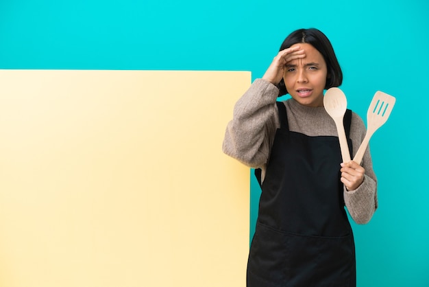 Giovane donna cuoca di razza mista con un grande cartello isolato su sfondo blu che guarda lontano con la mano per guardare qualcosa