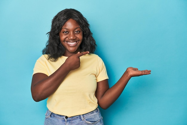 Giovane donna curvy afroamericana eccitata tenendo uno spazio di copia sul palmo