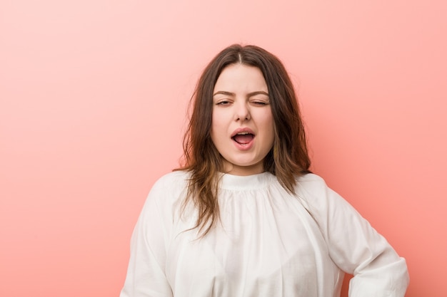 Giovane donna curvy caucasica che sta contro il fondo rosa