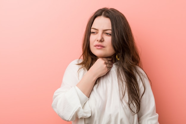 Giovane donna curvy caucasica che sta contro la parete rosa