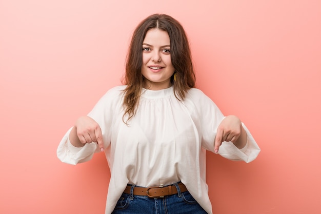 Giovane donna curvy caucasica che sta contro la parete rosa