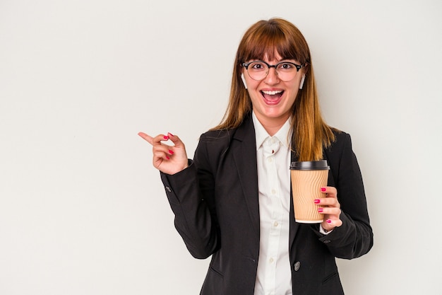 Giovane donna curvy caucasica di affari che tiene un caffè isolato su fondo bianco che sorride e che indica da parte, mostrando qualcosa allo spazio vuoto.