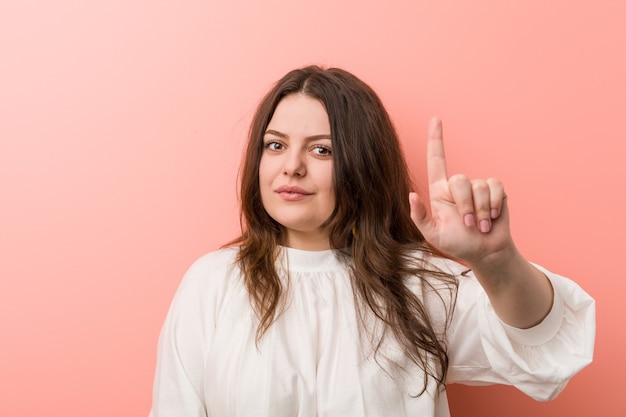 Giovane donna curvy caucasica in piedi contro sfondo rosa