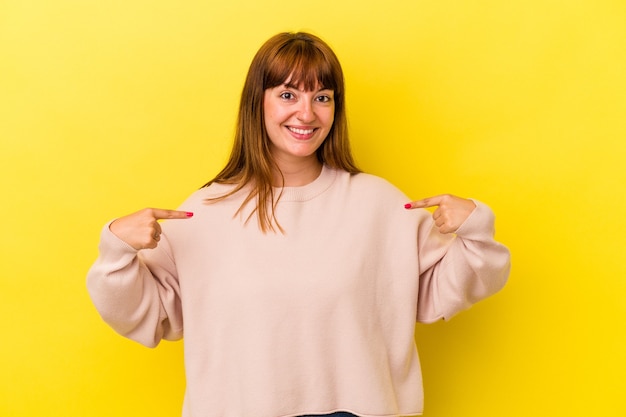 Giovane donna curvy caucasica isolata su sfondo giallo persona che indica a mano uno spazio copia camicia, orgogliosa e fiduciosa