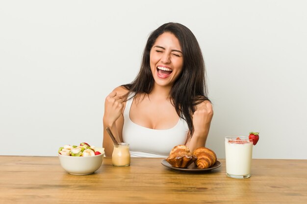 Giovane donna curvy che prende una colazione che incoraggia spensierata ed eccitata