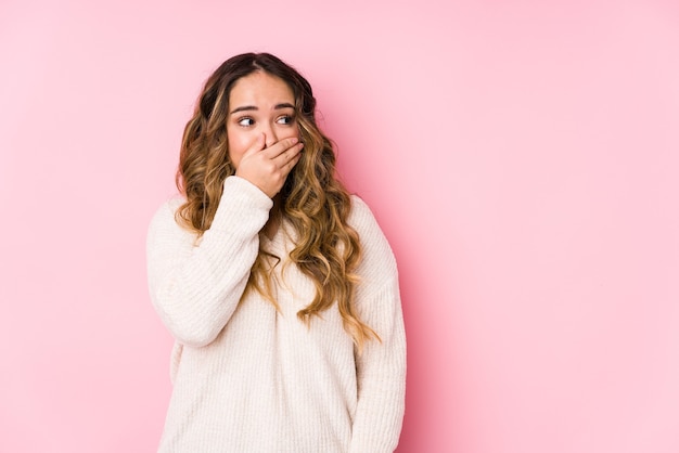 Giovane donna curvy in posa in un muro rosa isolato premuroso guardando uno spazio di copia che copre la bocca con la mano.