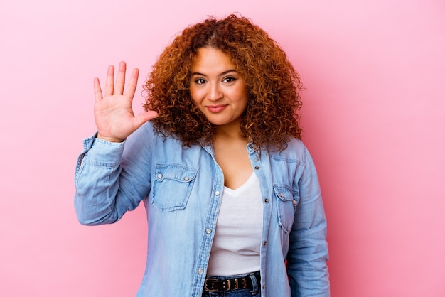 Giovane donna curvy latina isolata sul muro rosa sorridente allegro che mostra il numero cinque con le dita.