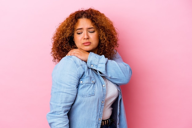 Giovane donna curvy latina isolata sulla parete rosa che ha un dolore alla spalla.