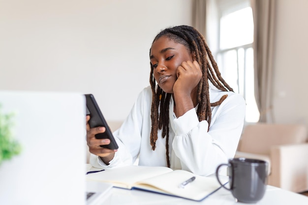 Giovane donna d'affari africana sorridente che utilizza smartphone vicino al computer in ufficio